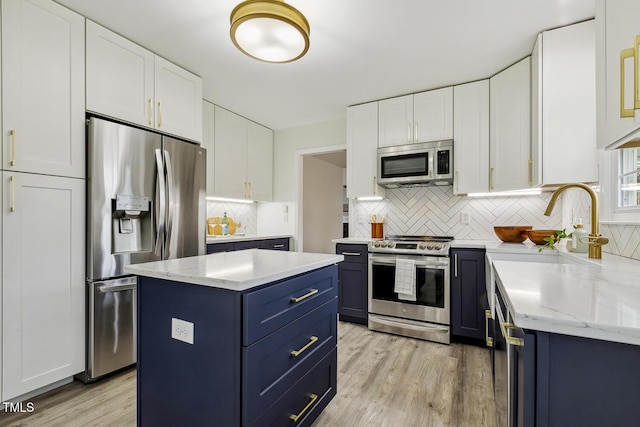 kitchen featuring appliances with stainless steel finishes, white cabinetry, a center island, blue cabinetry, and light hardwood / wood-style flooring