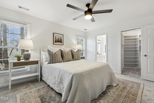 carpeted bedroom featuring ceiling fan, a spacious closet, ensuite bath, and a closet