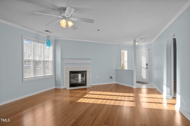 unfurnished living room with a tiled fireplace, light hardwood / wood-style floors, a wealth of natural light, and ornamental molding