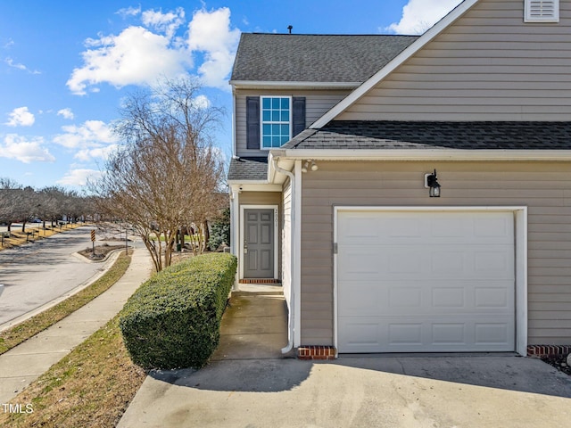 view of side of home with driveway, roof with shingles, and an attached garage