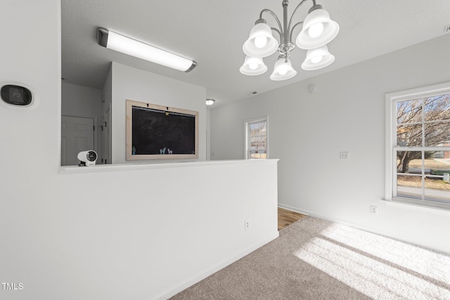 carpeted spare room with a notable chandelier and baseboards