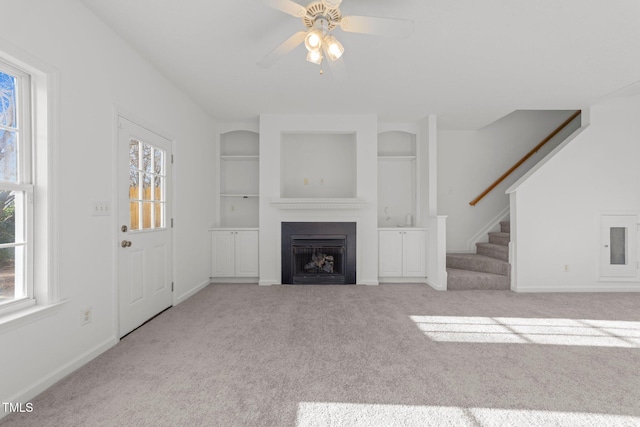 unfurnished living room featuring built in features, a healthy amount of sunlight, a fireplace, and light carpet