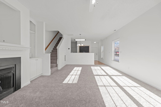 unfurnished living room with light carpet, a fireplace, stairway, and an inviting chandelier