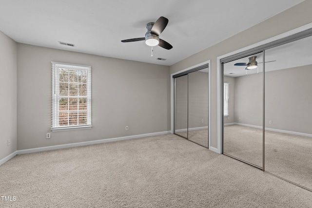 unfurnished bedroom featuring two closets, light colored carpet, and ceiling fan