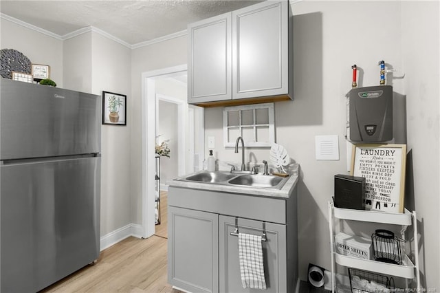 kitchen featuring stainless steel fridge, sink, gray cabinets, ornamental molding, and light hardwood / wood-style floors