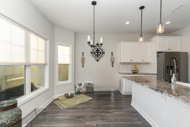 kitchen featuring hanging light fixtures, stainless steel fridge, white cabinets, and light stone counters