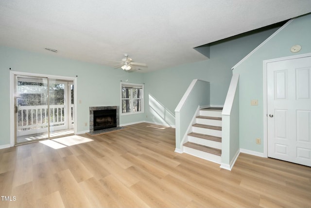 unfurnished living room featuring a tile fireplace, light wood-type flooring, a textured ceiling, and ceiling fan