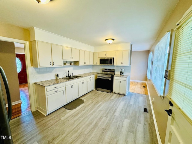 kitchen featuring light hardwood / wood-style floors, light stone countertops, appliances with stainless steel finishes, sink, and backsplash