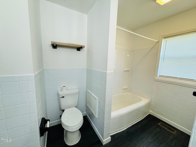 bathroom featuring toilet, shower / bathing tub combination, and tile walls