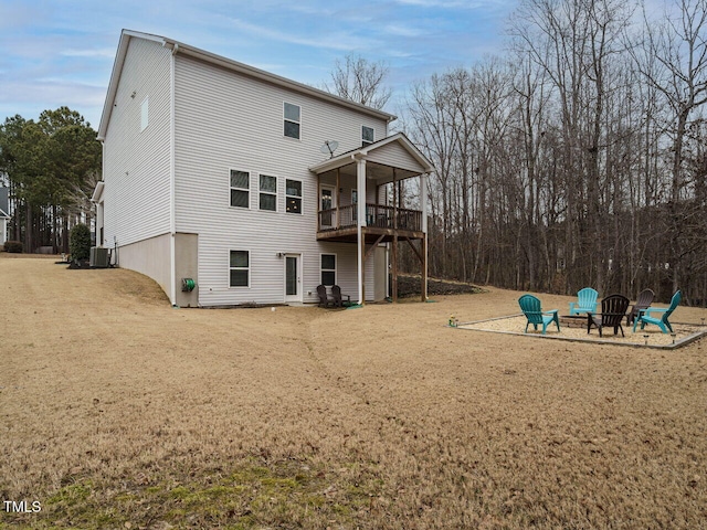 rear view of property with a balcony, an outdoor fire pit, central AC, and a yard