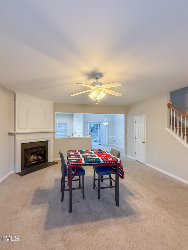 dining space featuring carpet floors, a large fireplace, and ceiling fan