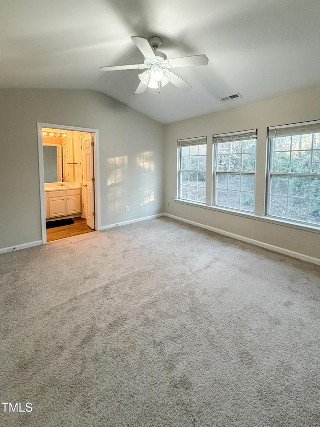 unfurnished bedroom featuring multiple windows, connected bathroom, vaulted ceiling, and light colored carpet