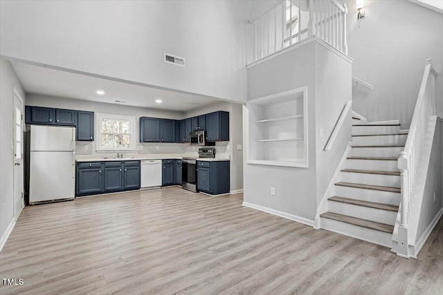 kitchen featuring appliances with stainless steel finishes, a towering ceiling, built in features, blue cabinets, and light wood-type flooring