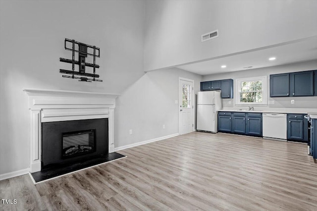 unfurnished living room featuring sink, a towering ceiling, and light wood-type flooring