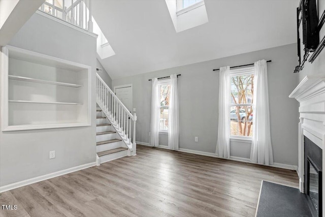 unfurnished living room with built in shelves, a skylight, light hardwood / wood-style floors, and a healthy amount of sunlight