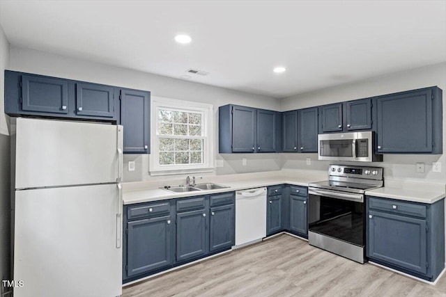 kitchen with appliances with stainless steel finishes, blue cabinets, sink, and light wood-type flooring