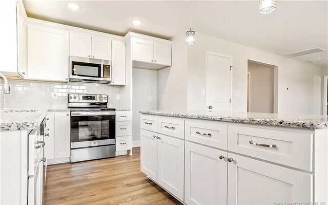 kitchen with decorative light fixtures, light wood-type flooring, tasteful backsplash, white cabinetry, and stainless steel appliances