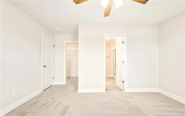 unfurnished bedroom with ceiling fan, light carpet, a closet, and a walk in closet