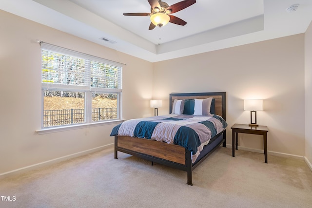 bedroom with light colored carpet, ceiling fan, and a raised ceiling