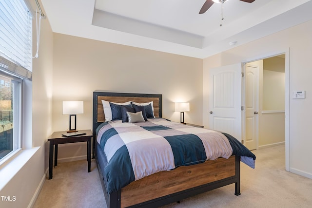 bedroom with ceiling fan, light colored carpet, and a tray ceiling