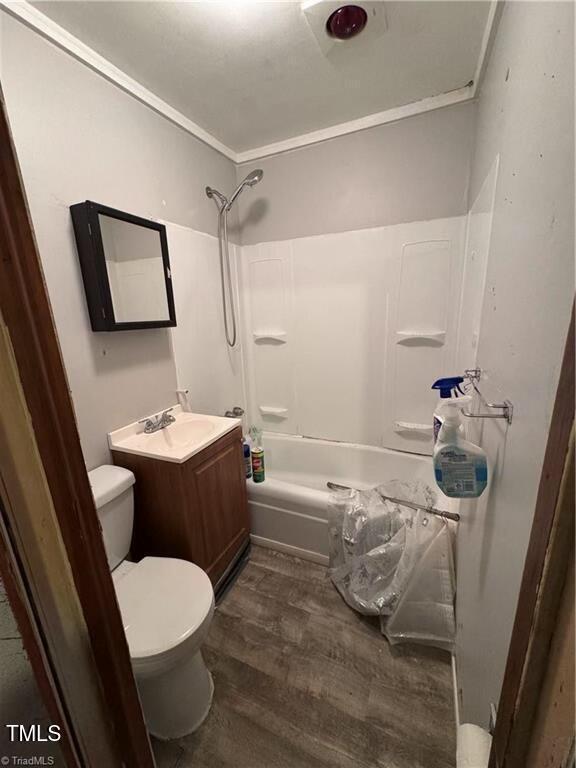 full bathroom with ornamental molding, hardwood / wood-style flooring, toilet, and washtub / shower combination