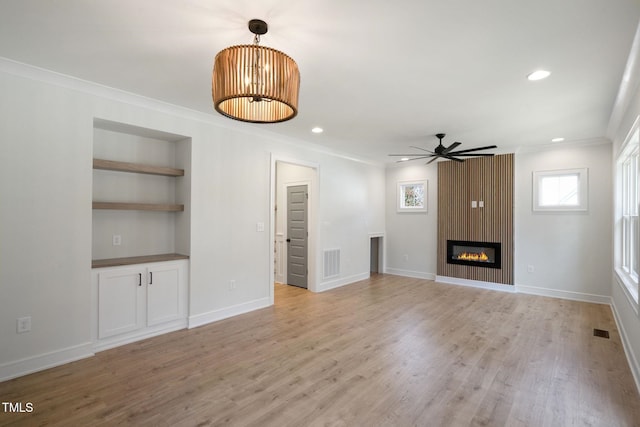 unfurnished living room featuring built in shelves, crown molding, light hardwood / wood-style flooring, a large fireplace, and ceiling fan