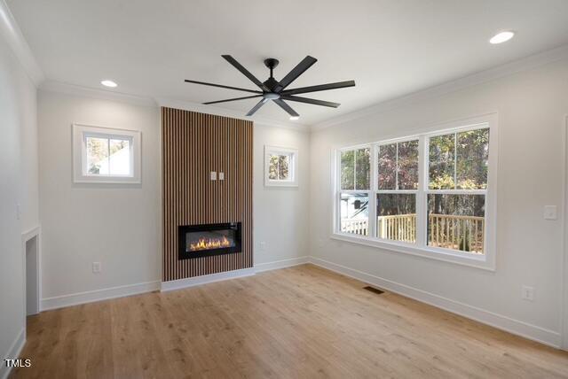 unfurnished living room featuring crown molding, light hardwood / wood-style flooring, a large fireplace, and ceiling fan