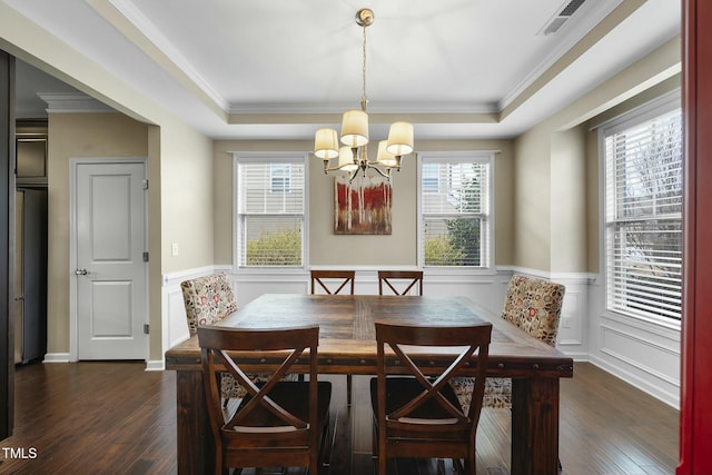 dining space with dark wood-type flooring, ornamental molding, and a raised ceiling