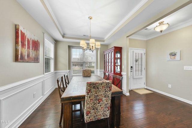 dining area with dark wood-type flooring, ornamental molding, a raised ceiling, and a notable chandelier