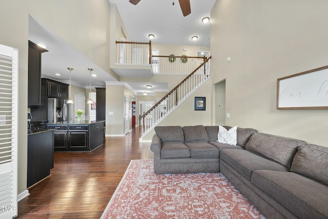 living room featuring a towering ceiling, dark wood-type flooring, ornamental molding, and ceiling fan