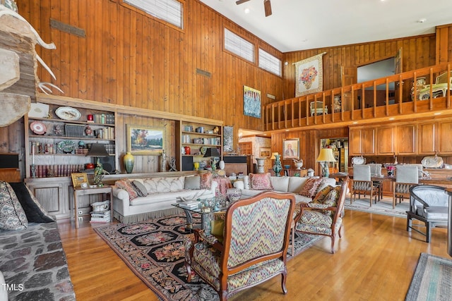 living room featuring built in features, light wood-type flooring, a towering ceiling, and ceiling fan