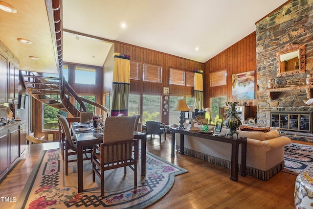 dining space featuring hardwood / wood-style flooring, high vaulted ceiling, wooden walls, and a fireplace