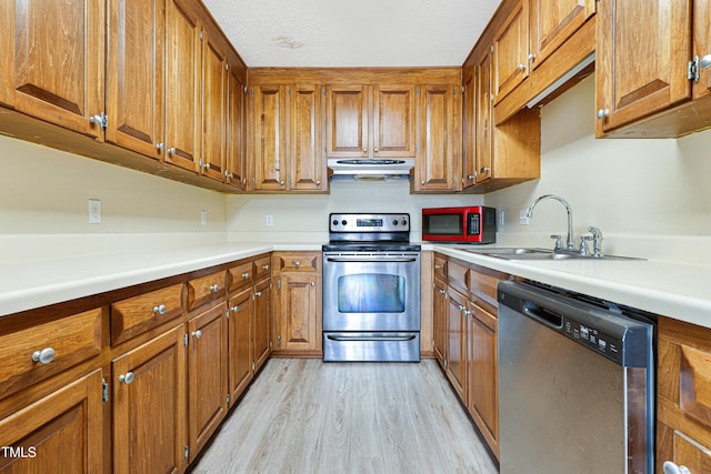 kitchen with sink, light wood-type flooring, a textured ceiling, and appliances with stainless steel finishes