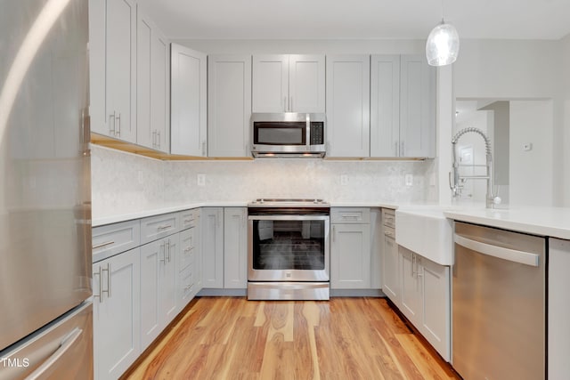 kitchen with sink, stainless steel appliances, decorative backsplash, decorative light fixtures, and light wood-type flooring