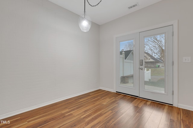 unfurnished room with hardwood / wood-style flooring, brick wall, and french doors