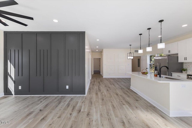 kitchen with sink, hanging light fixtures, light hardwood / wood-style floors, white cabinets, and stainless steel fridge with ice dispenser