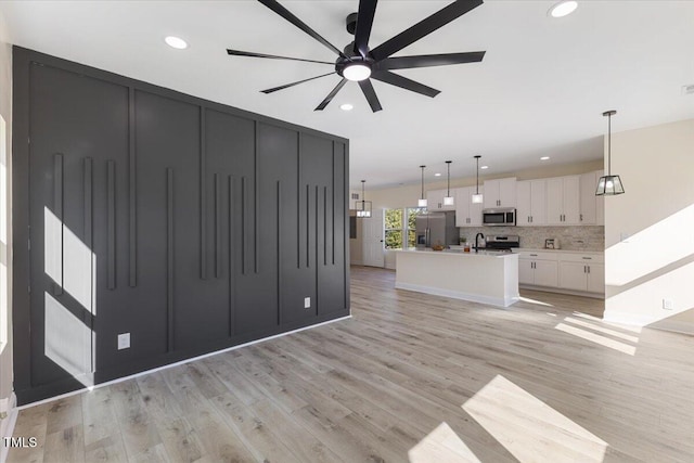 unfurnished living room with ceiling fan, sink, and light wood-type flooring