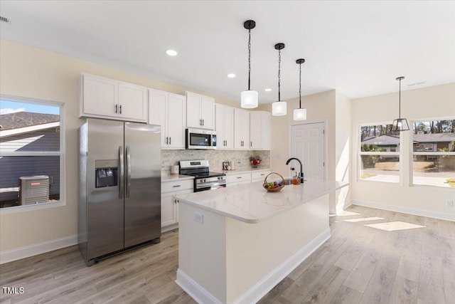 kitchen with white cabinetry, tasteful backsplash, a center island with sink, stainless steel appliances, and light stone countertops