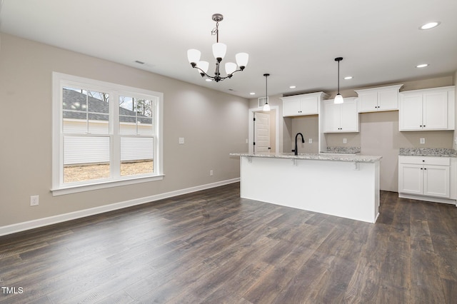 kitchen with decorative light fixtures, a center island with sink, and white cabinets