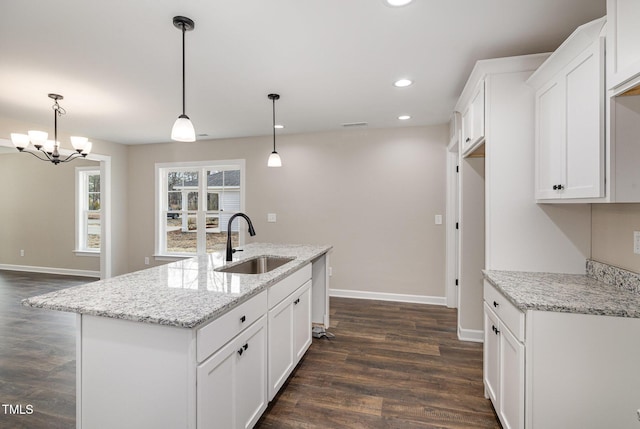 kitchen featuring sink, white cabinetry, light stone counters, pendant lighting, and a kitchen island with sink