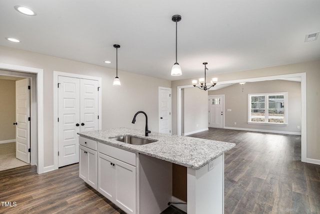 kitchen featuring pendant lighting, sink, white cabinetry, light stone counters, and an island with sink