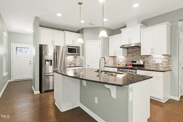 kitchen with sink, decorative light fixtures, dark stone counters, stainless steel appliances, and a kitchen island with sink