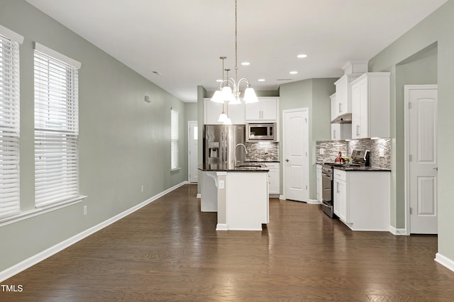 kitchen with appliances with stainless steel finishes, an island with sink, sink, white cabinets, and hanging light fixtures