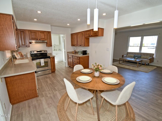 kitchen featuring sink, light hardwood / wood-style flooring, a textured ceiling, appliances with stainless steel finishes, and pendant lighting