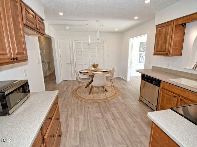 kitchen featuring pendant lighting, sink, appliances with stainless steel finishes, a textured ceiling, and light wood-type flooring