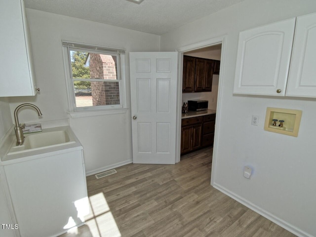 washroom featuring sink, hookup for a washing machine, cabinets, a textured ceiling, and light wood-type flooring