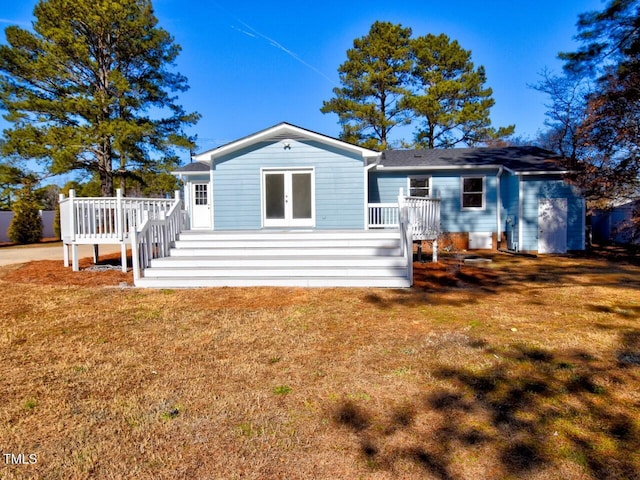 rear view of house featuring a wooden deck, a lawn, and french doors