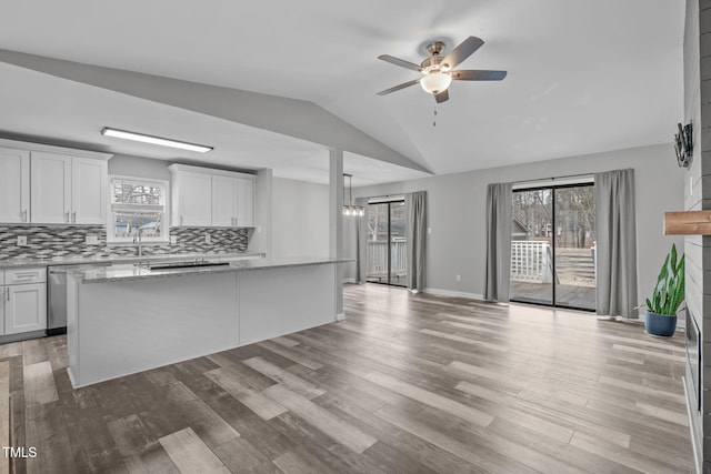 kitchen featuring white cabinets, backsplash, vaulted ceiling, and light stone countertops