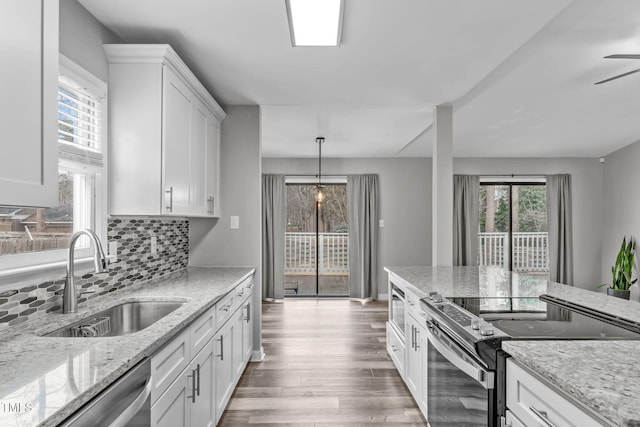 kitchen with white cabinetry, stainless steel appliances, sink, backsplash, and light stone counters