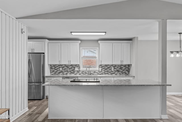 kitchen featuring white cabinets, vaulted ceiling, light stone counters, and stainless steel fridge